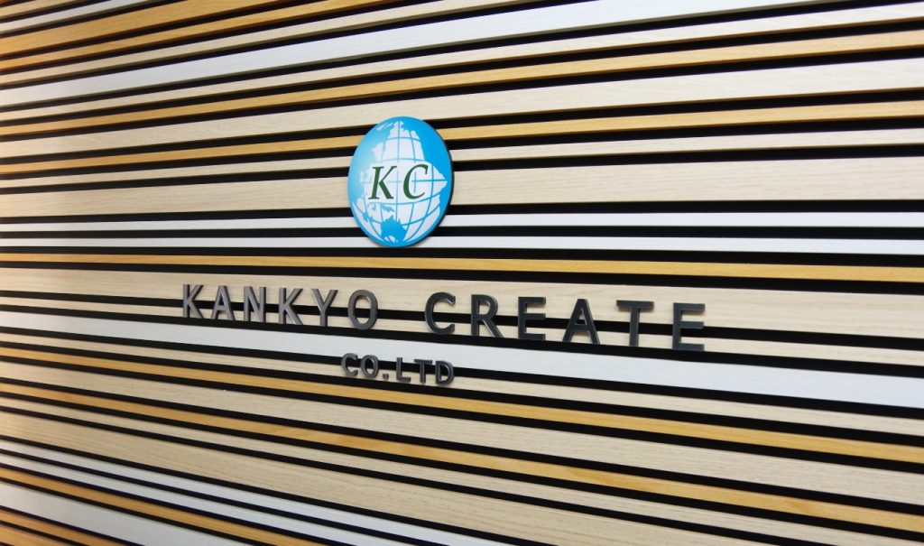 ストライプ柄の壁に、水色の地球をモチーフにした環境クリエイト株式会社のロゴマークと、英語表記の社名がデザインされています。