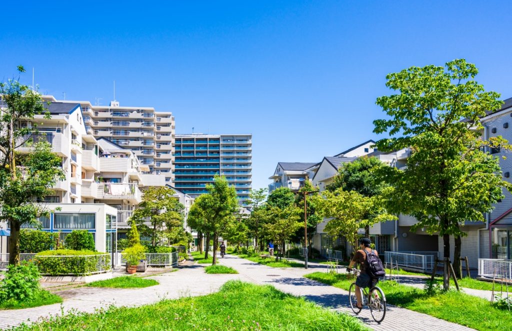 マンションや戸建て住宅に囲まれた緑豊かな遊歩道をサイクリングする人